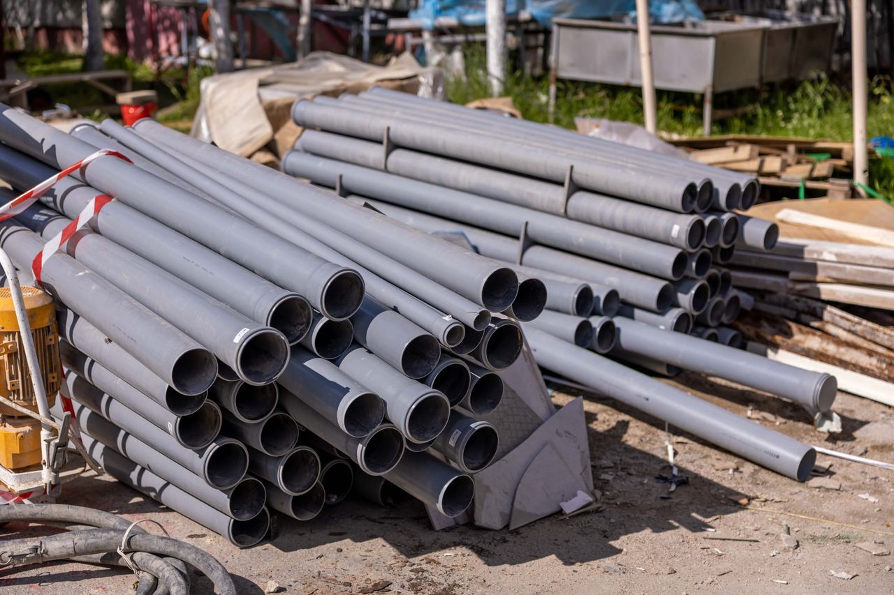 services-03 A collection of gray PVC pipes neatly stacked at an outdoor construction site.